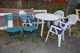 A white plastic garden table and four chairs with blue cushions, plus two plastic folding chairs.
