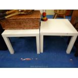 A pair of square white occasional tables.