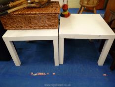 A pair of square white occasional tables.