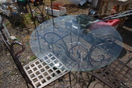 An ornate iron based glass topped table and three chairs, 3' 7 1/2" diameter x 2' 3 1/2" high.