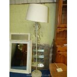 A cream metal standard lamp with glass droppers and cream shade.