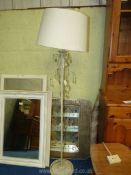 A cream metal standard lamp with glass droppers and cream shade.