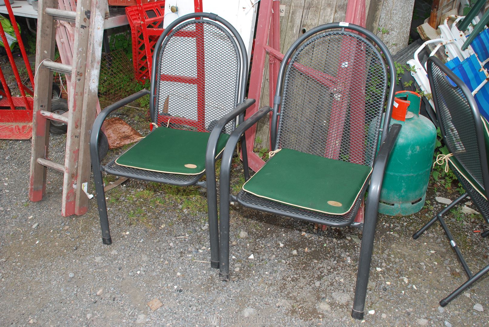 A pair of metal garden chairs with green and cream cushions.