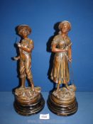 Two cast metal figures on plinths, one of a boy holding a scythe,