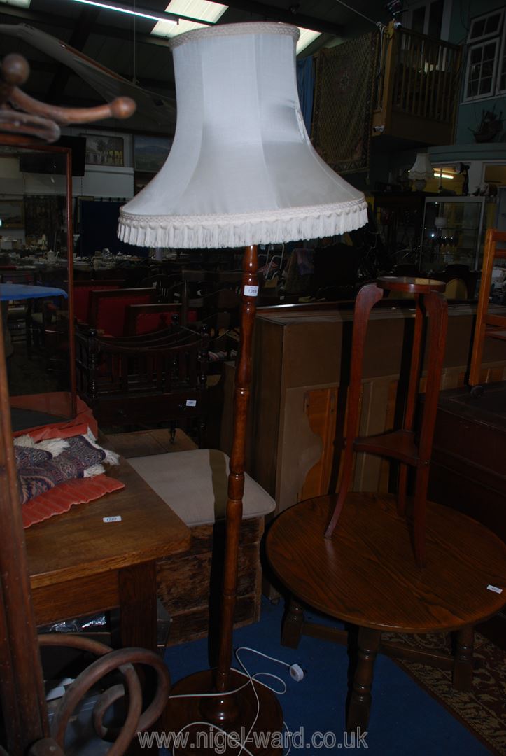 A wooden standard lamp with cream fringed shade (tear to shade) standing on 3 flat round feet.