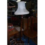 A wooden standard lamp with cream fringed shade (tear to shade) standing on 3 flat round feet.