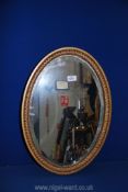 An oval bevelled wall mirror in gold painted wooden frame, 15" wide x 21" high.