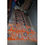Two rugs, one in orange ground with blue stylized flowers, the other dark blue ground with orange,