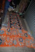 Two rugs, one in orange ground with blue stylized flowers, the other dark blue ground with orange,