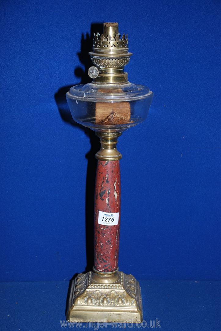 An Oil lamp on square brass bass, marbled effect stand, clear glass reservoir, no shade or chimney,