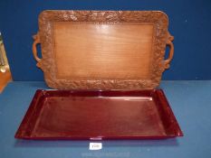 A carved wooden tray having two handles and a long red plastic tray.