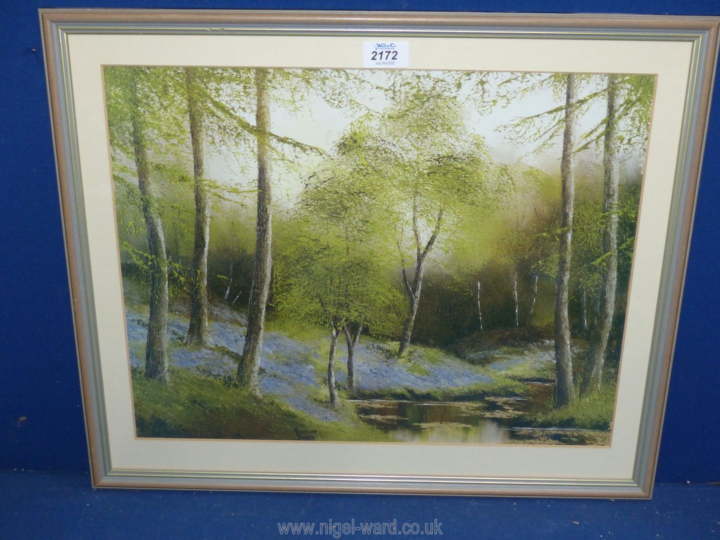 A framed and mounted Print depicting a woodland with stream and bluebells, signed Madeline Ronco.
