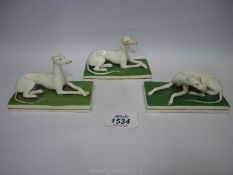 Three small Staffordshire porcelain greyhounds on green rectangular bases, two in lying position,