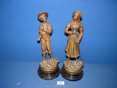 Two cast metal figures on plinths, one of a boy holding a scythe,