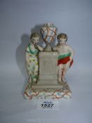 A Staffordshire porcelain figure of a girl and boy leaning on a plinth having an orange and blue