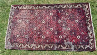 A red ground well worn Eastern rug decorated with interlocking medallions and foliate border, a/f.