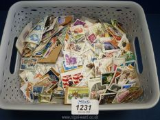 A plastic tub containing world stamps, some mounted on paper.