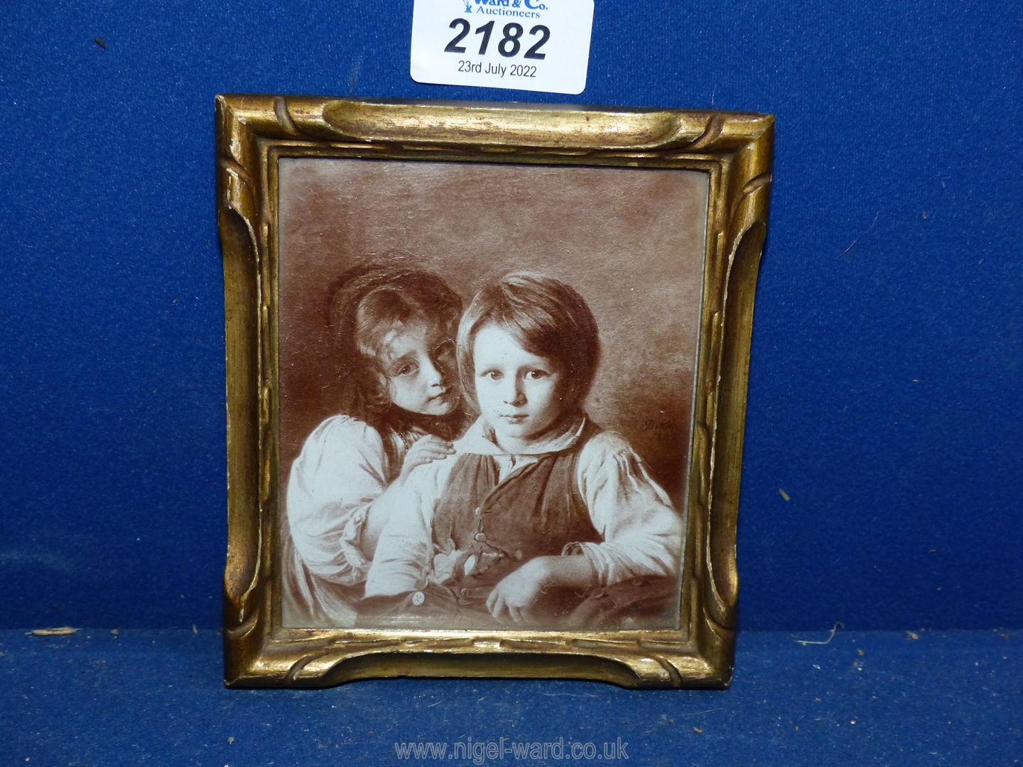 A gold coloured frame containing a sepia Photograph of a portrait of a young girl & boy in early