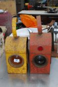 Two vintage metal railway lamps, one red and the other orange.