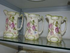 Three graduated jugs in pink rose pattern, with middle jug having a chip.