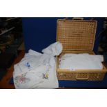 A picnic basket containing small and medium linen tablecloths,