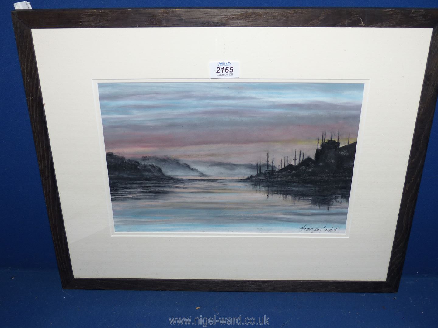 A framed and mounted watercolour depicting a coastal scene at sunset,