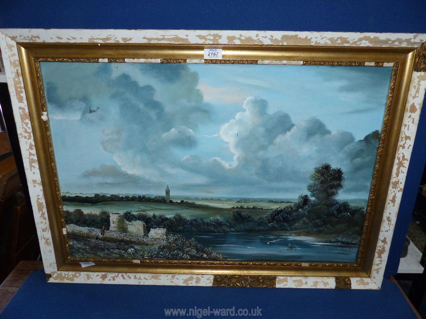 A large oil on canvas depicting a river landscape with a figure walking past castle ruins and a