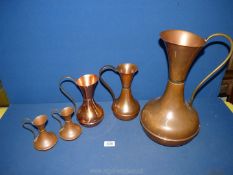 Five copper graduated pitchers, various sizes.