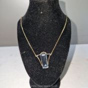 A art deco gold pendant on chain hallmarked 9 carat and set with a baguette cut transparent blue