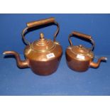 A large copper kettle with acorn finial and one smaller kettle.