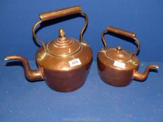 A large copper kettle with acorn finial and one smaller kettle.