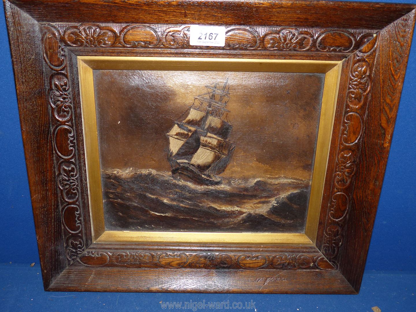 A carved wooden framed Oil on canvas depicting a sailing vessel on high seas in brown tones,