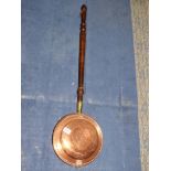 A copper bed warming pan with turned wood handle.