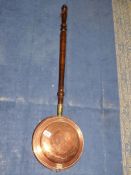 A copper bed warming pan with turned wood handle.