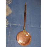 A copper warming pan with brass hinges and brass and wood handle.