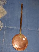 A copper warming pan with brass hinges and brass and wood handle.