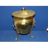 A brass lidded urn on three legs with paw feet and three handles, lid very bent and dented,