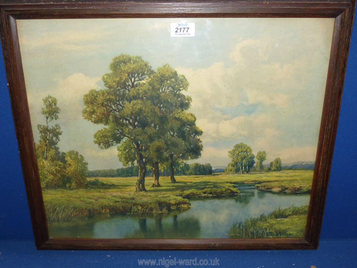A wooden framed print depicting a river scene with fields, trees and rolling hills in the distance,