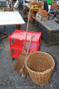 A red painted 3 tier trolley on castors, wicker basket, axe and broom.