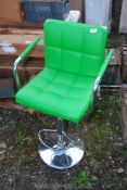 A bar stool with green faux leather seat.