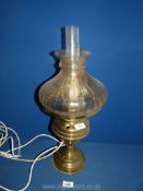 An Oil Lamp converted to electric with a brass base with a tinted orange shade and clear chimney,