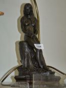 A lamp base with figure of a lady holding flowers, on a wooden base, with shade.