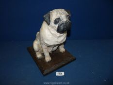 A pottery sculpture of a white seated Pug on a wooden plinth, 12" tall (a/f).