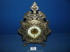 An ornate brass framed Clock with central panel depicting cherub figure with castle in the distance,