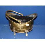 A brass coal bucket with four feet and handle.
