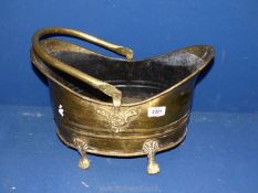 A brass coal bucket with four feet and handle.