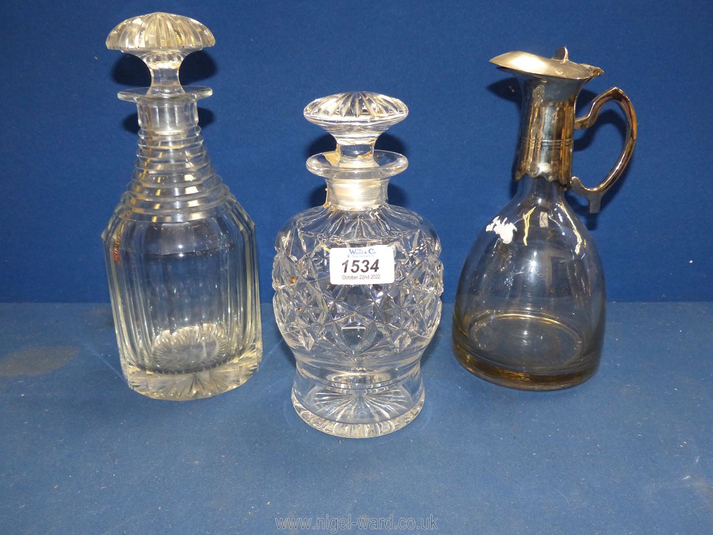 Two cut glass decanters and a modern claret jug with unmarked white metal collar and spout.
