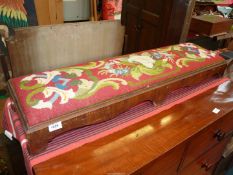 A long Victorian kneeler with floral pattern tapestry cover in red, white, green and blue, 43" long.