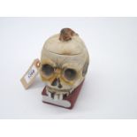 A scarce late 19th century biscuit porcelain 'scholar's' tobacco jar in the form of a skull resting