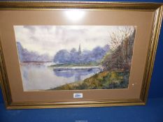 A framed and mounted watercolour depicting a river landscape with a Church spire peaking out of the